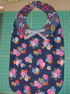 a blue floral bib with a bow on the front, and a green cutting board behind it