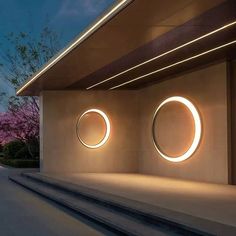 two circular lights on the side of a building with steps leading up to it and trees in the background