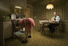 an older man and woman are looking into the open oven in their kitchen at night