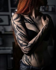 a woman with red hair and tattoos on her chest is posing for the camera in a dark room