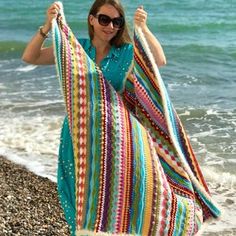 a woman holding up a colorful blanket on the beach