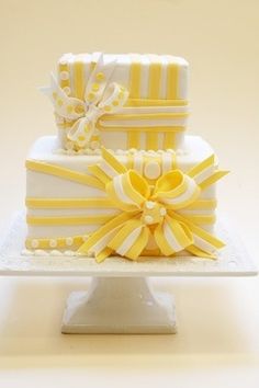 a three tiered cake with yellow and white ribbons on it's sides, sitting on a plate