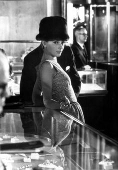 a woman in a dress and hat standing at a counter with other people behind her