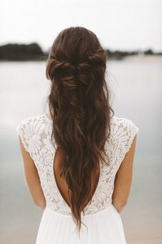 a woman with long hair standing on the beach looking out at the water and holding her back to the camera