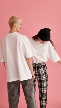 two people standing next to each other in front of a pink wall wearing white shirts and plaid pants