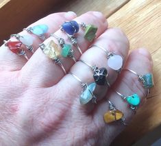 a person's hand holding several rings with different colored stones on them, all in various shapes and sizes