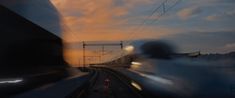 a blurry photo of a train going down the tracks at sunset or dawn with power lines in the foreground