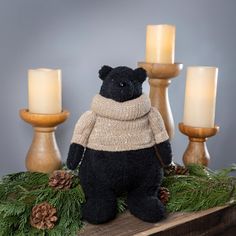 a black teddy bear sitting on top of a table next to candles and pine cones