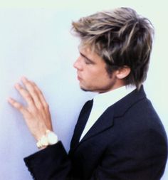 a man in a suit and tie leaning against a wall with his hand on the wall