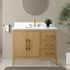 a bathroom vanity with marble counter top and gold faucet, next to a potted plant