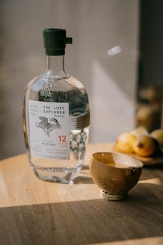 a bottle of alcohol sitting on top of a wooden table next to a small bowl