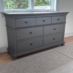 a gray dresser sitting in front of a window next to a carpeted area with a rug on the floor