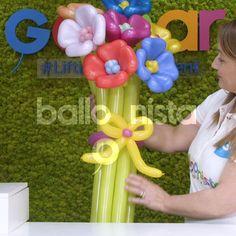 a woman standing next to a tall balloon flower display in front of a green wall