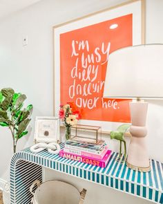 a desk with a lamp, vase and pictures on the wall in front of it