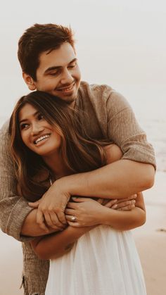 a man and woman hugging each other on the beach