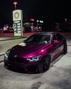 a purple car is parked in front of a gas station at night with the lights on