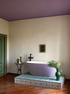 a bath tub sitting on top of a wooden floor next to a table with a potted plant