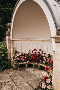 a bench with flowers on it sitting in front of a white wall and doorways