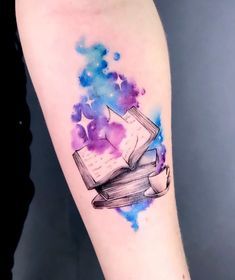 a watercolor tattoo with an open book on the arm