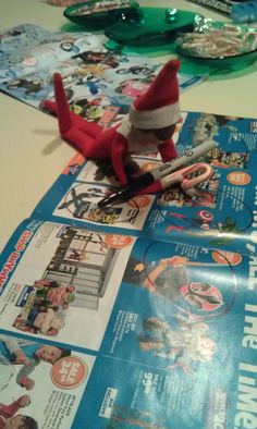 an elf is sitting on top of a magazine with scissors in his hand, and the other