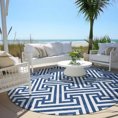 an outdoor living area with white furniture and blue rugs on the floor next to the ocean