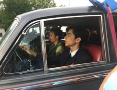 two young men sitting in the back seat of a car, looking out the window