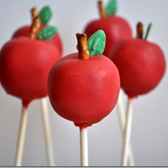 four red apples with green leaves on them sitting on top of toothpick sticks