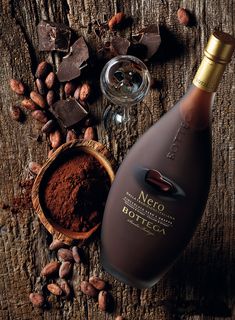 a bottle of wine sitting next to some nuts and chocolate on a wooden table with a spoon