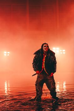 a man standing in the water with his hands on his hips wearing a clown mask