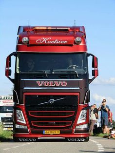 a red volvo truck driving down a road with people standing on the side of it