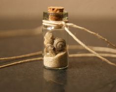 a small glass bottle filled with sand and a snail on it's side, next to twine of twine