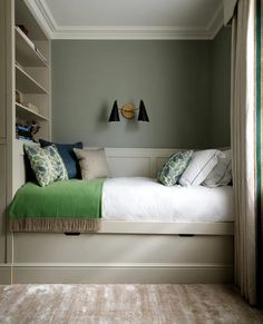 a bed sitting under a window next to a book shelf