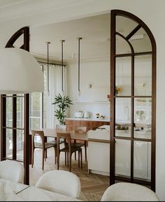 an open kitchen and dining room area with white walls, wood flooring and large arched windows