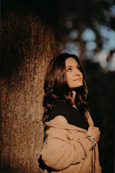 a woman standing next to a tree with her arms wrapped around the tree's trunk