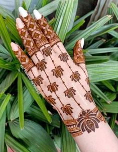 a woman's hand with henna on it and green leaves in the background