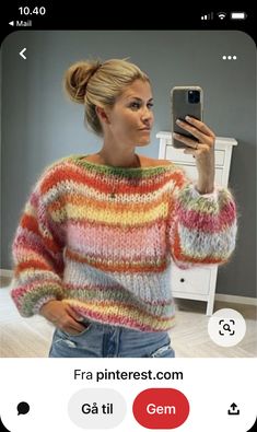 a woman taking a selfie in front of a mirror wearing a colorful sweater and jeans