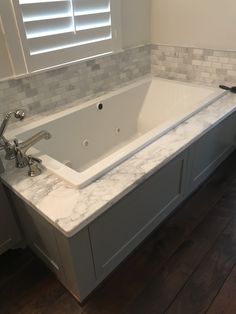 a large white bath tub sitting on top of a wooden floor next to a window