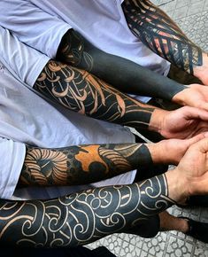 three men with tattoos on their arms holding each other's hands while sitting down