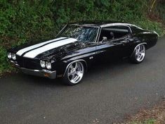 a black and white muscle car parked on the side of a road next to some bushes