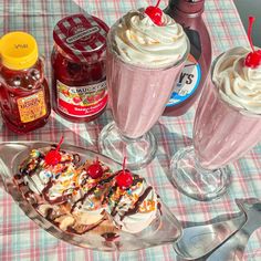 ice cream sundaes with whipped cream and cherries are on a picnic table