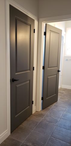 two gray doors are open in a room with tile flooring and white trim on the walls