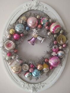 a christmas wreath with ornaments hanging from it's side on a wall in a white frame