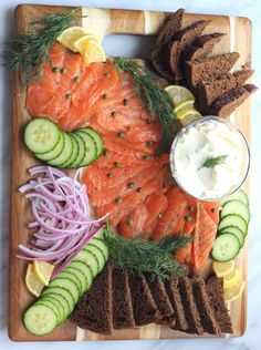 a wooden cutting board topped with sliced up salmon and cucumbers next to bread