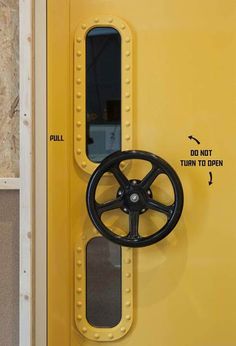 a yellow door with a black wheel attached to the front and side panels that are labeled do not turn to open