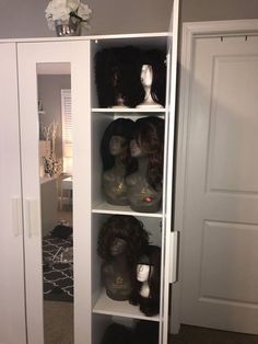 several wigs are displayed on shelves in a room with white doors and carpeting