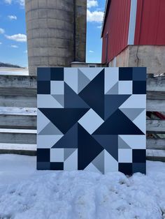 a blue and white quilt sitting in the snow next to a red silo on a farm