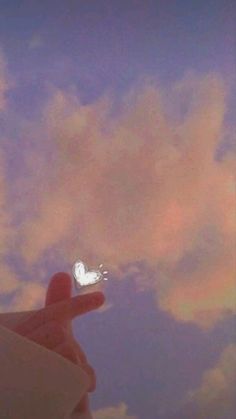 a hand holding a tiny white heart shaped object in front of a cloudy blue sky