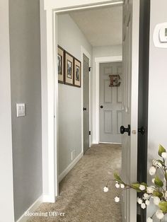 an empty hallway leading to a white door with pictures on the wall and flowers in vase