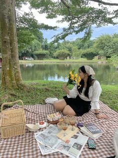 a woman sitting on top of a picnic table next to a lake with flowers in her hand