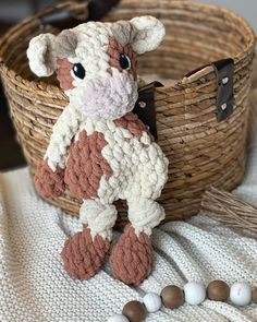 a knitted cow sitting in front of a basket with beads on the floor next to it